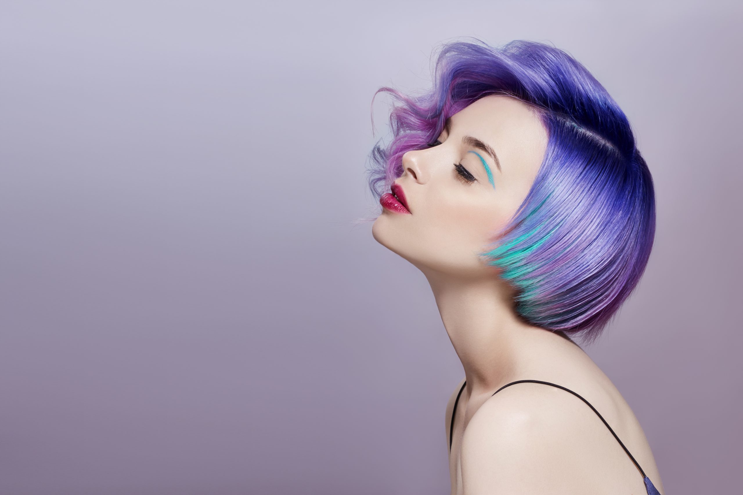 Portrait of a woman with bright colored flying hair, all shades of purple. Hair coloring, beautiful lips and makeup. Hair fluttering in the wind. Sexy girl with short  hair. Professional coloring